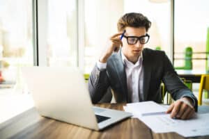 Happy man entering data from home on laptop an office work place